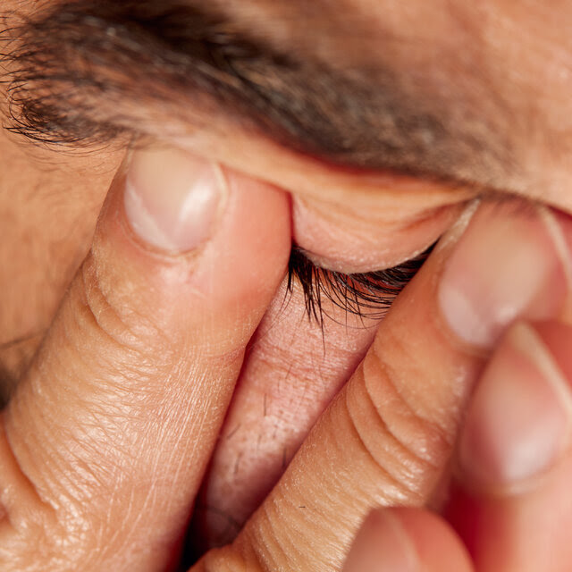 A photograph of a man rubbing his eyes.