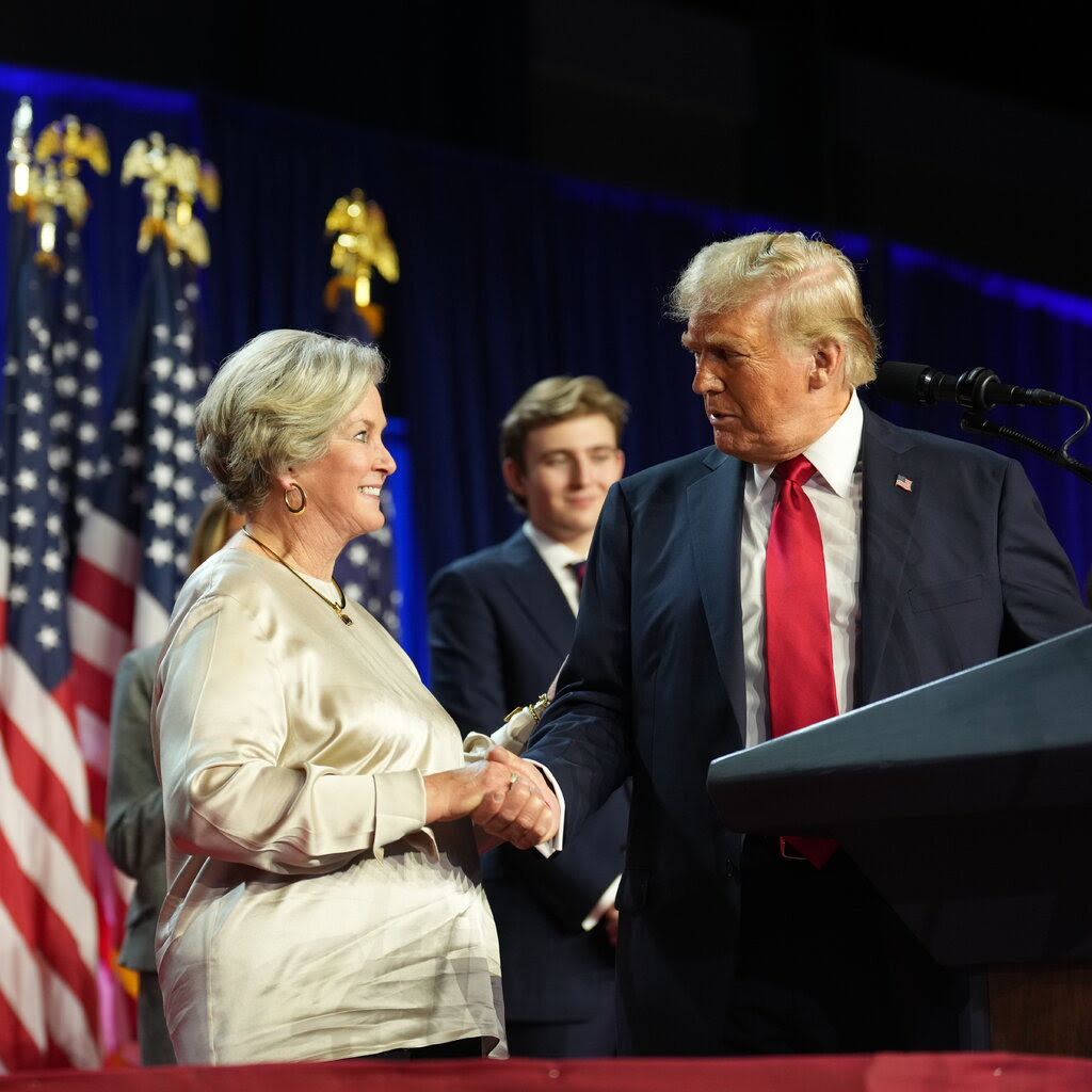 Donald Trump shakes the hand of a woman in a gold silk shirt.