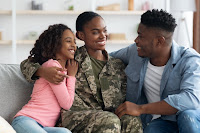 A military family smiles while sitting at home, thinking about their financial future.