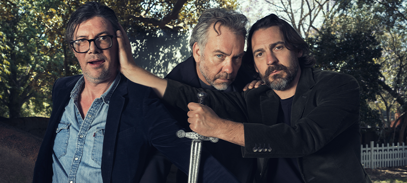 three men posing for a photo with a sword