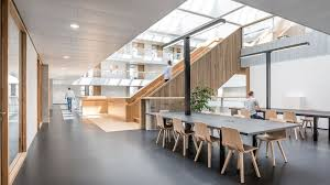 multi-level office environment with natural wood accents, open communal working tables, and a minimalist design that emphasizes functionality and natural light, creating an inviting modern workspace.