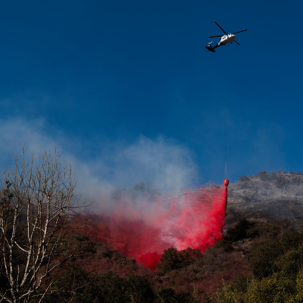 A fire helicopter drops fire retardant on trees on the side of a hill.