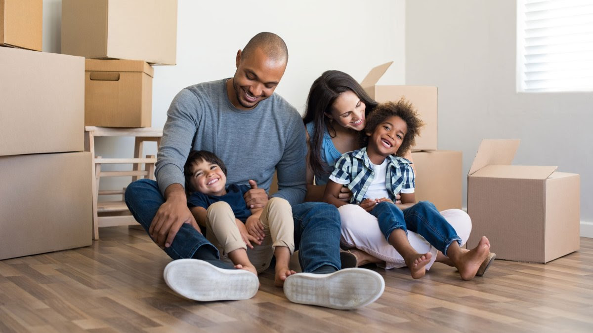 A family sits in their new home smiling and laughing surrounded by moving boxes