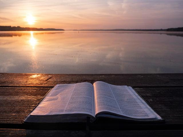 Bible open in front of a sunset by the water