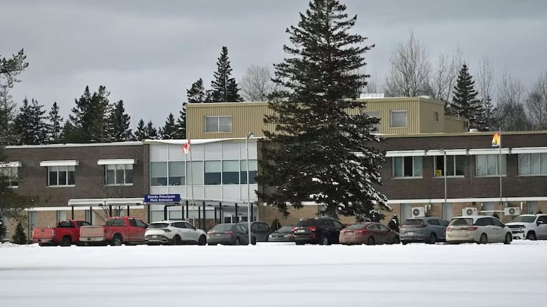 A winter scene of a mostly brick building, with several vehicles in the parking lot.