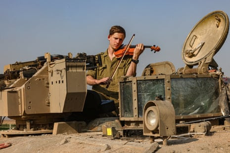 An Israeli soldier in Israel on the border near Gaza, playing a violin on a tank