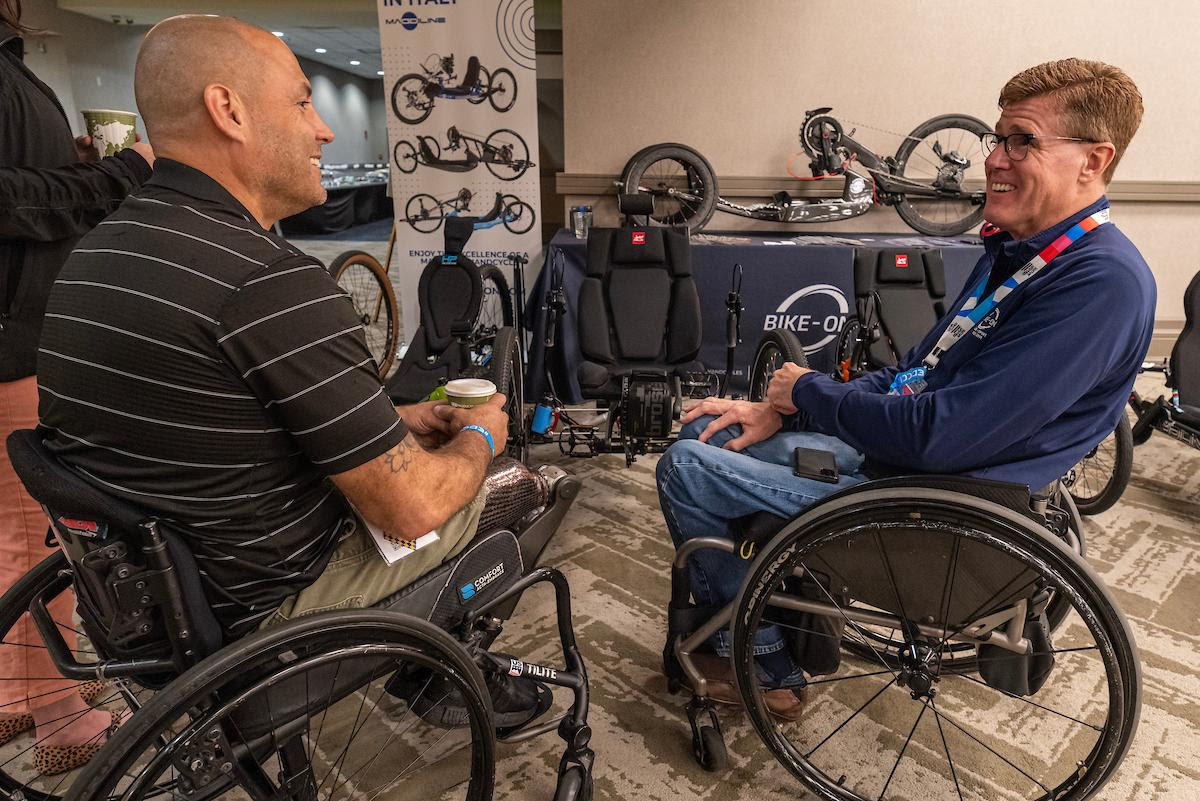 two individuals facing each other speaking with bike adaptive bike equipment in background