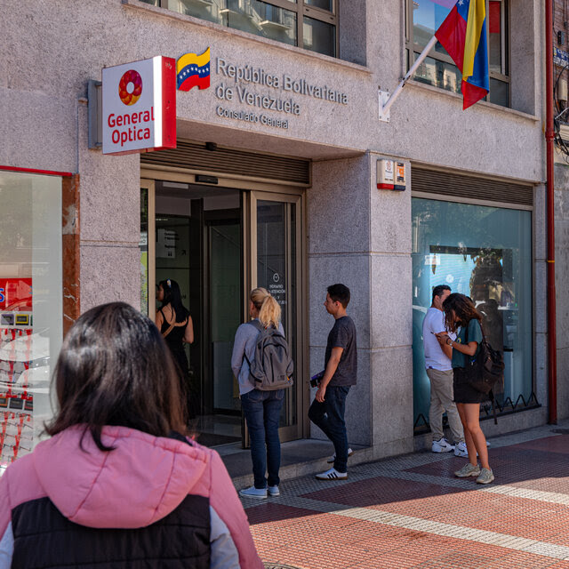 People line up outside an office building flying the flag of Venezuela.