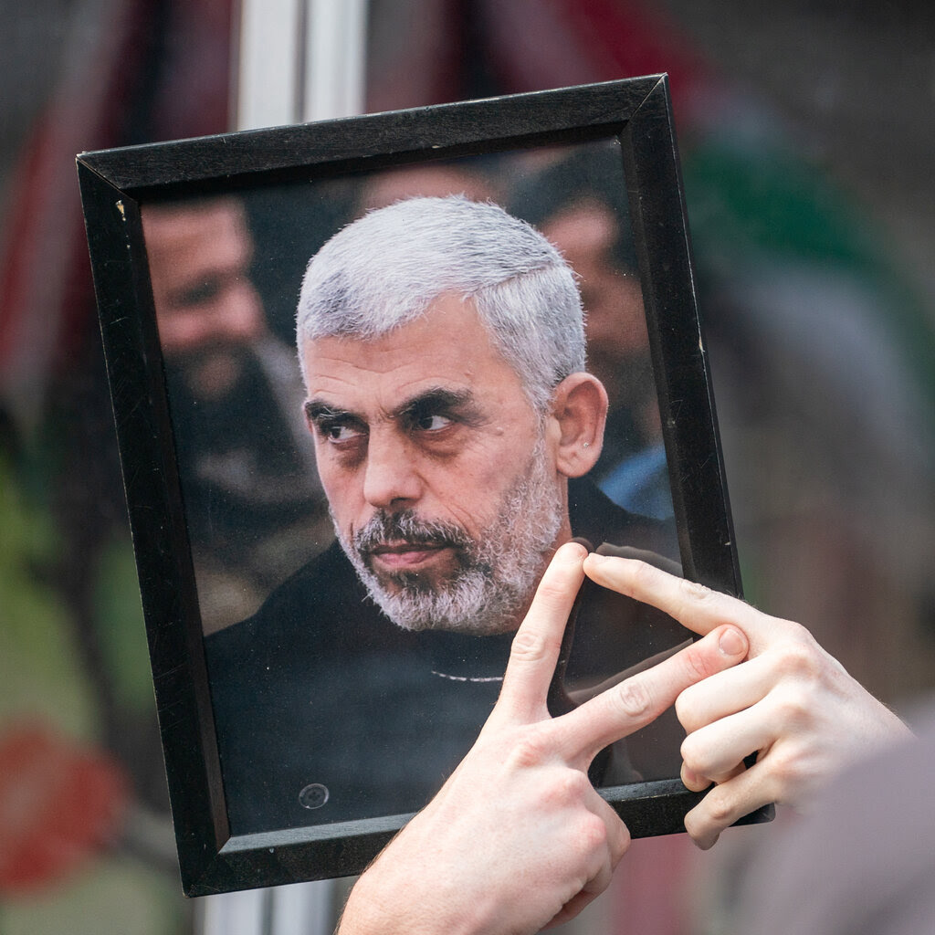 A pair of hands holds up a framed image of Yahya Sinwar. 