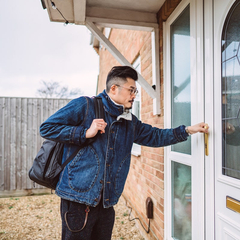 Young man with a backpack opening the front door of his house. 