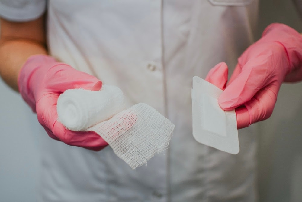 Healthcare professional wearing pink gloves holding traditional gauze and an adhesive wound dressing, illustrating different wound care options.