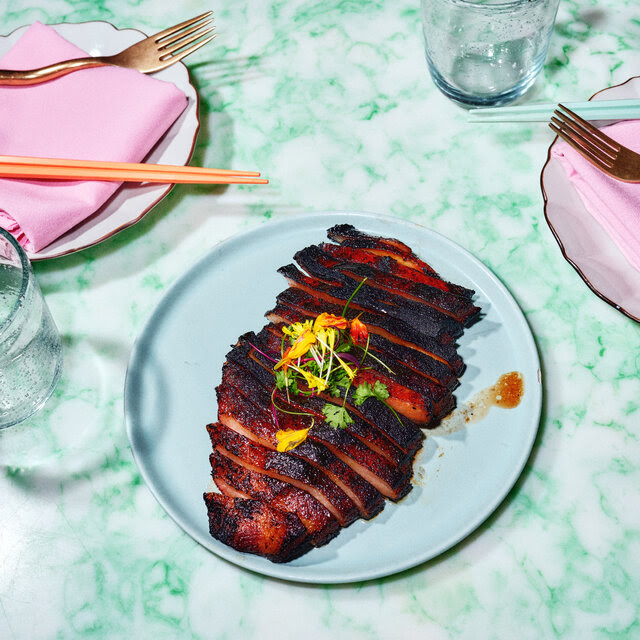 A colorful restaurant table with a dish of sliced roast pork.