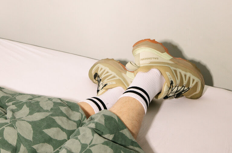 Feet wearing sneakers stick out from underneath the covers on a bed.