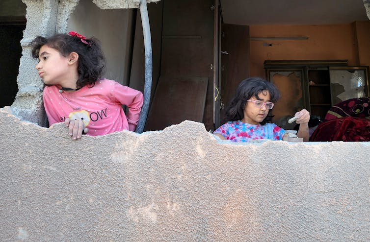 Two girls look out of a hole in the side of a building