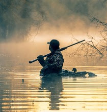 Hunter with decoys in water at sunrise