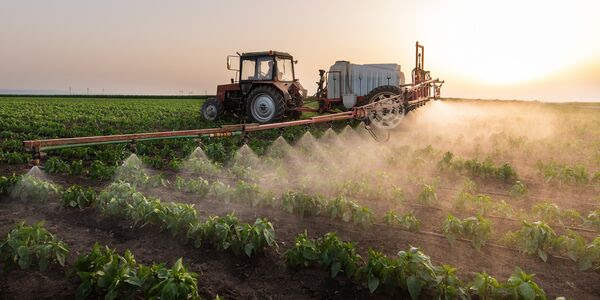 A tractor sprays fertilizer over a farm.