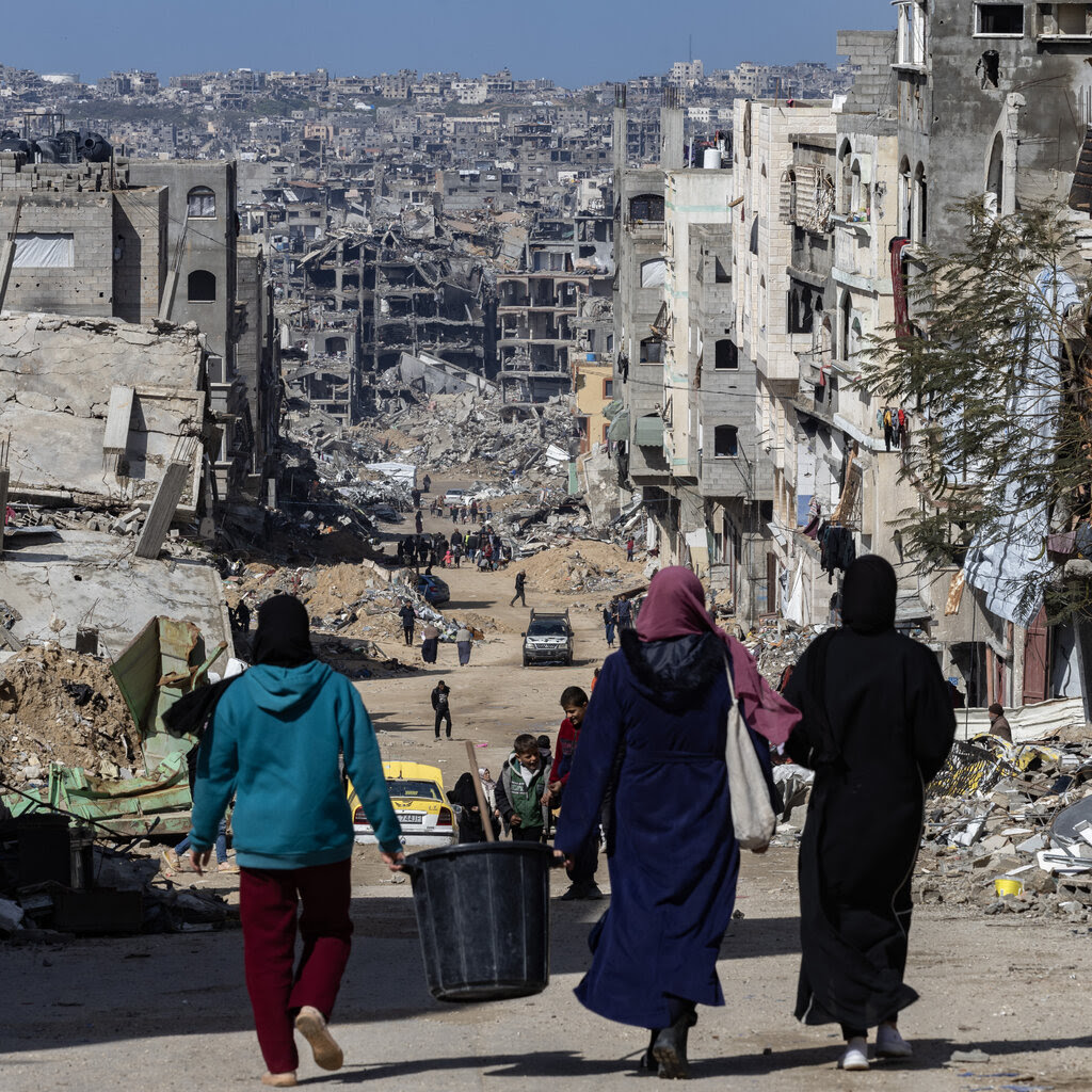 Three people walking down a hill with a destroyed city in the distance.