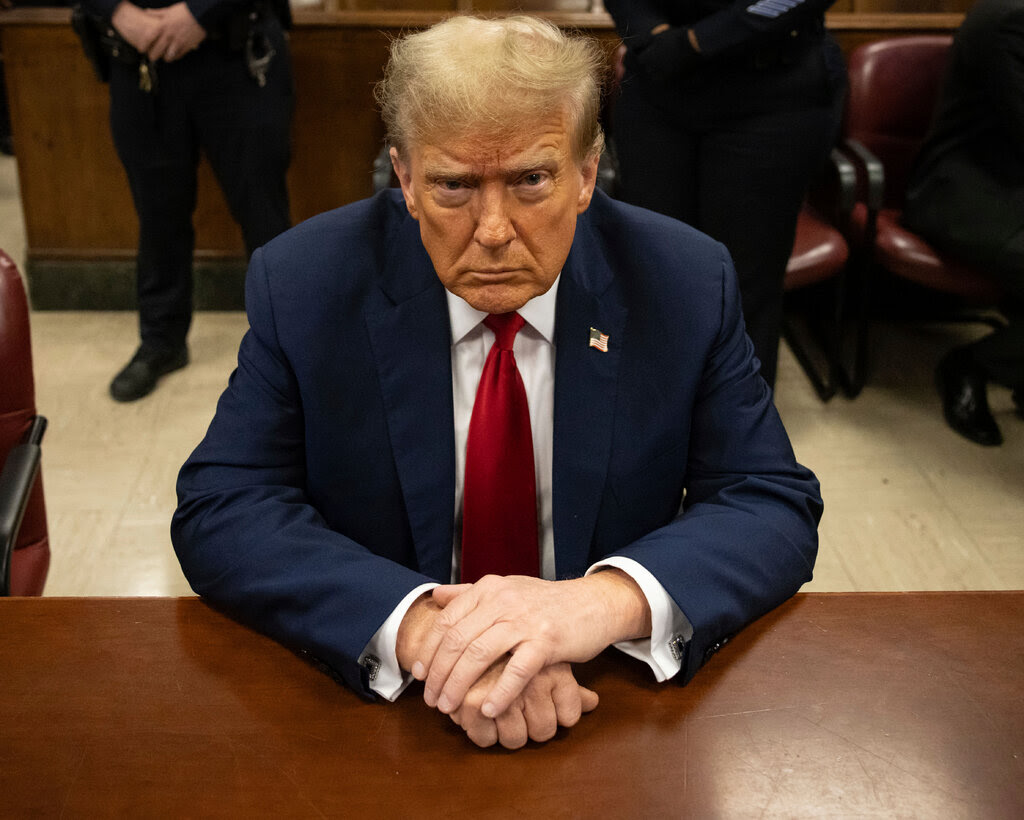 Donald Trump wearing a suit and a red tie sitting in a courtroom. 