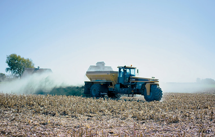 A tractor spreads crushed basalt over a recently-harvested cornfield.