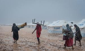 Las mujeres llevan sus pertenencias a través del suelo fangoso en un lugar de reunión para desplazados internos cerca de Kassala, Sudán.