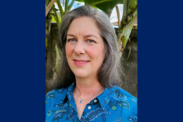 Sarah Malloy smiles wearing a blue patterned shirt. The image has two dark blue borders on either side.