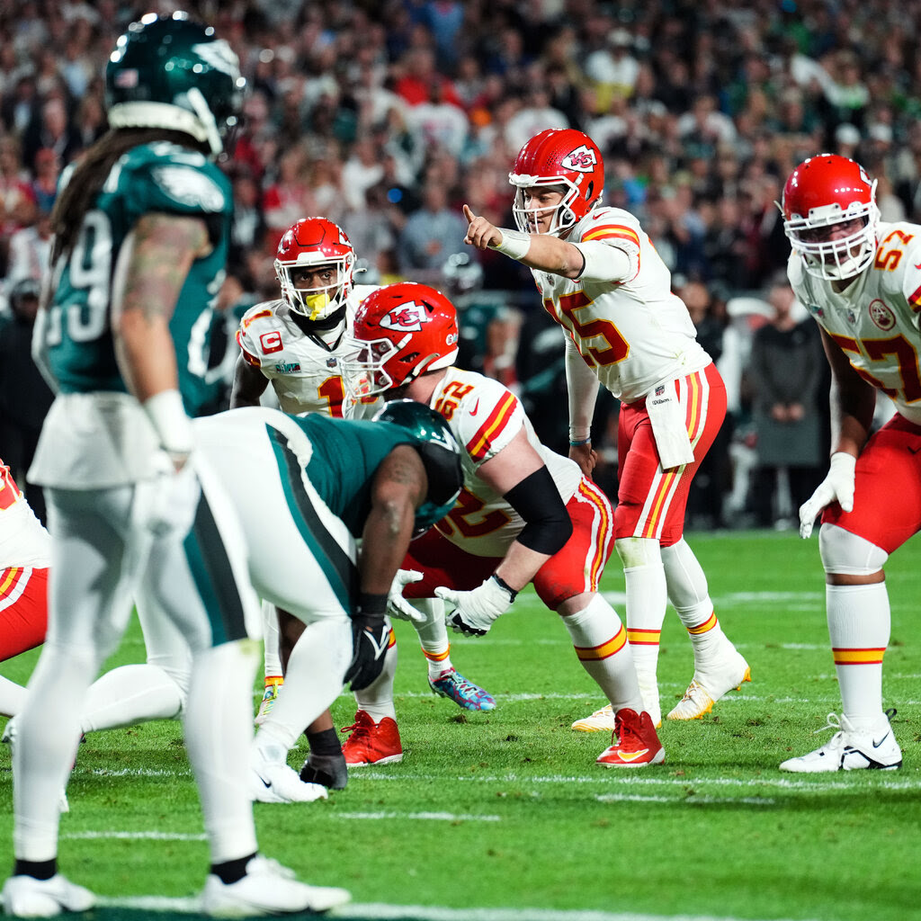 Patrick Mahomes hodling up one finger in a signal as other players prepare to clash.