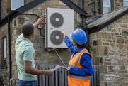 People looking at a air source heat pump on back of a building