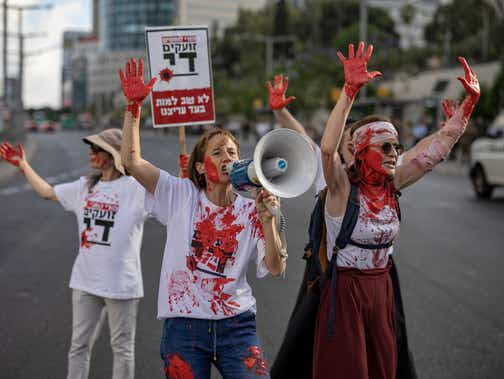 Mothers of combat soldiers who are serving in the Gaza Strip, covered with red paint, block a road demanding the end of the war, in Tel Aviv on Wednesday.