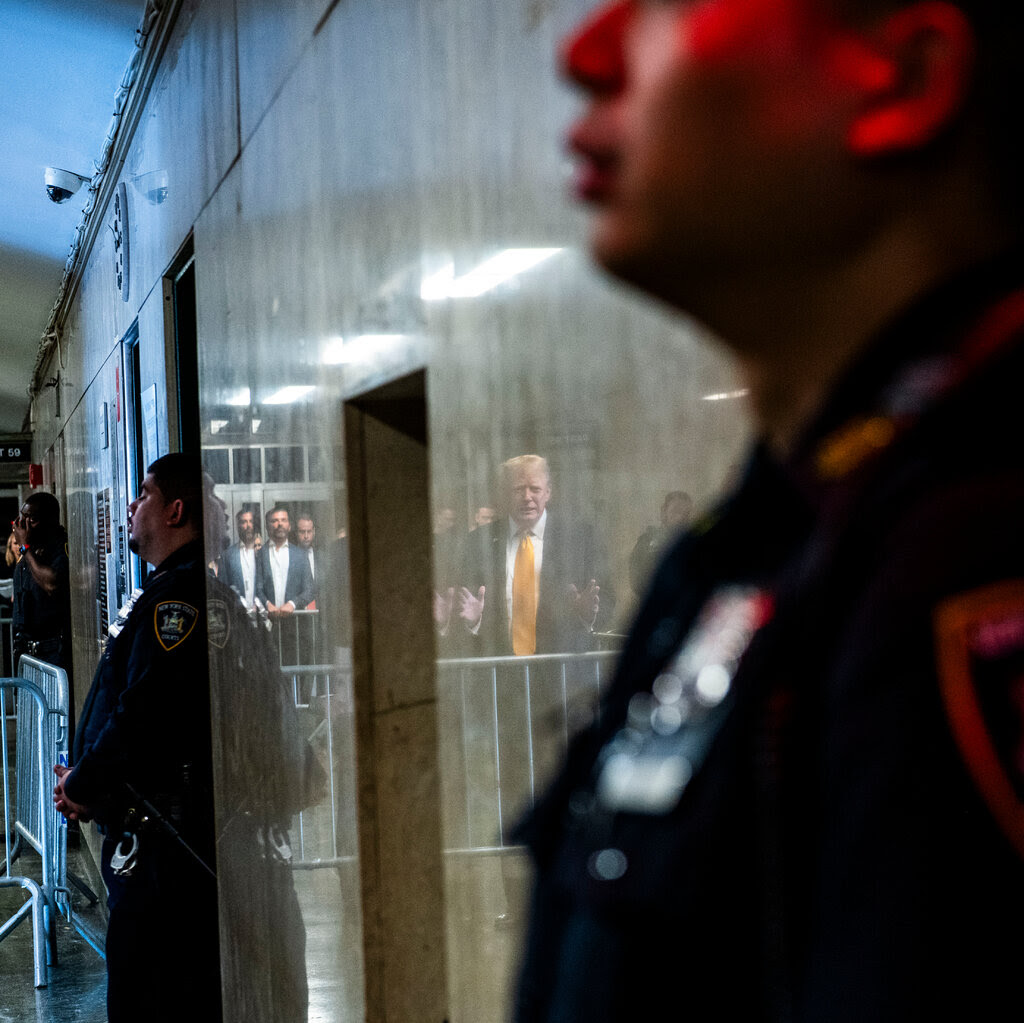 Donald Trump’s reflection is seen on the wall of the Manhattan courthouse, while police officers stand by. 