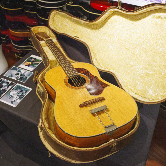 An acoustic guitar sits in an open padded case on a table. 