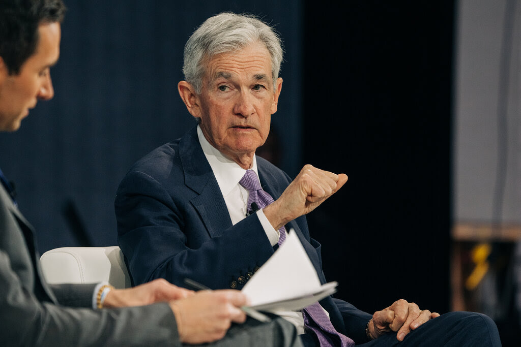 Jerome H. Powell gestures with one hand while sitting in a chair on a stage and talking with Andrew Ross Sorkin, who is partly visible.