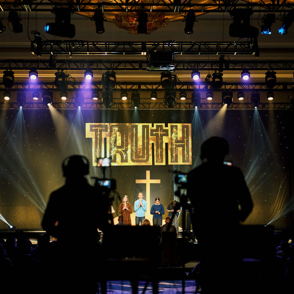 A stage with children clasping their hands under a cross and a sign that reads “truth.”