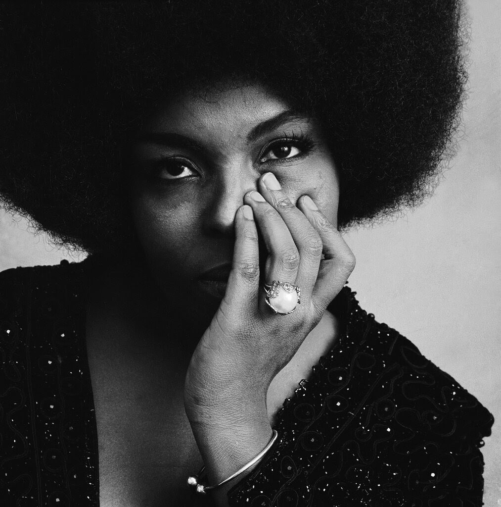 A black and white close-up portrait of Roberta Flack. One hand cups her chin and touches her nose. 