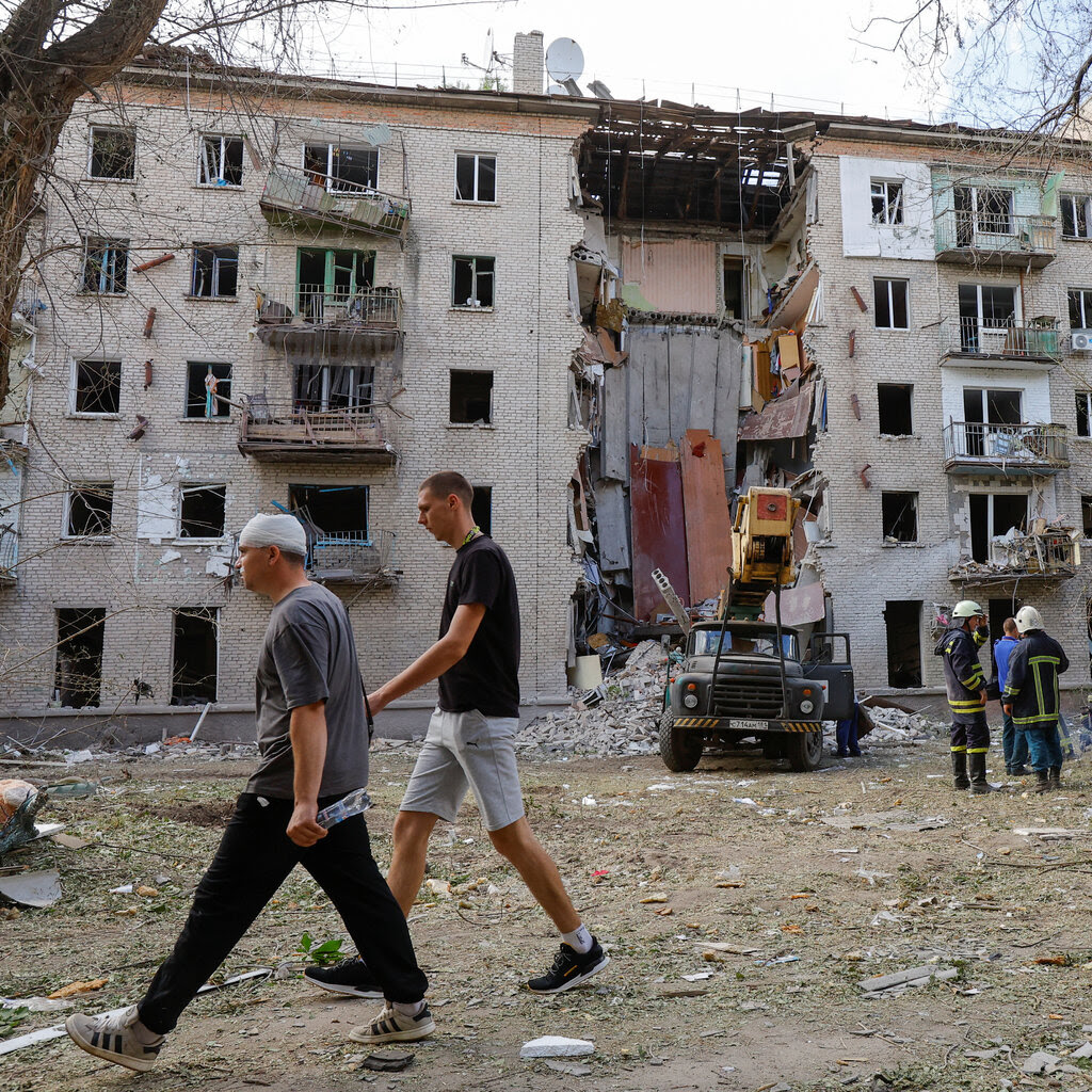 Two men walk by a bombed building. 