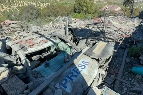 Getty Images Due SUV gravemente danneggiati, con finestrini rotti e telai accartocciati. Uno ha la parola "press" scritta sul cofano. Macerie e metallo contorto sono ammucchiati sopra e intorno.