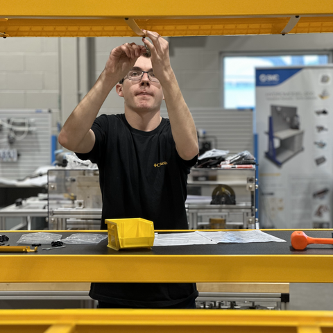 a student reaches up with a tool to adjust a bolt on a beam