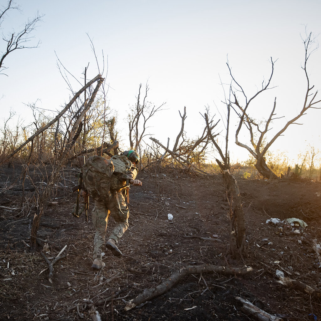 A soldier walks up a hill covered in dead and broken trees.