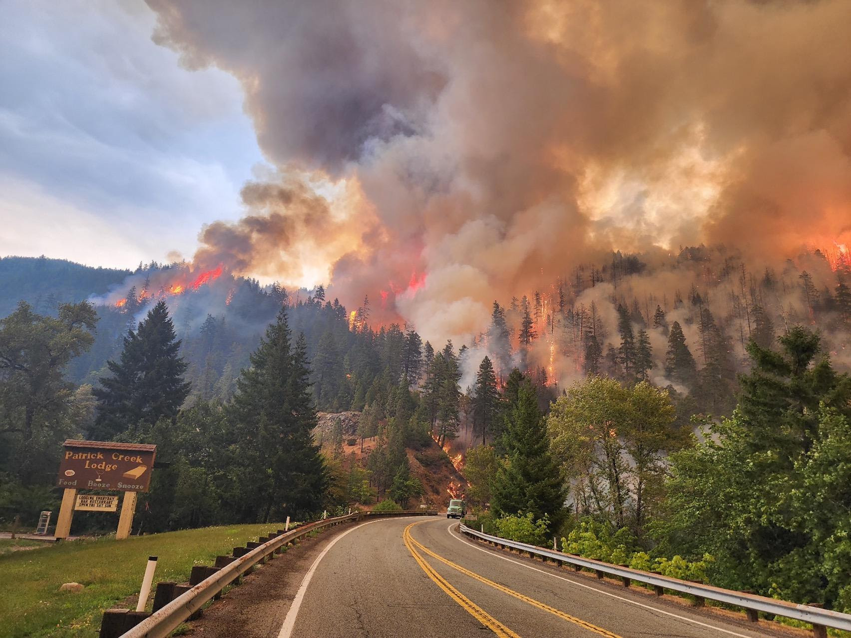 Billowing smoke over a fiery forest with road leading in.