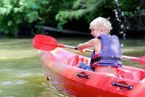 a young boy in a red kayak on water is paddling away from camera