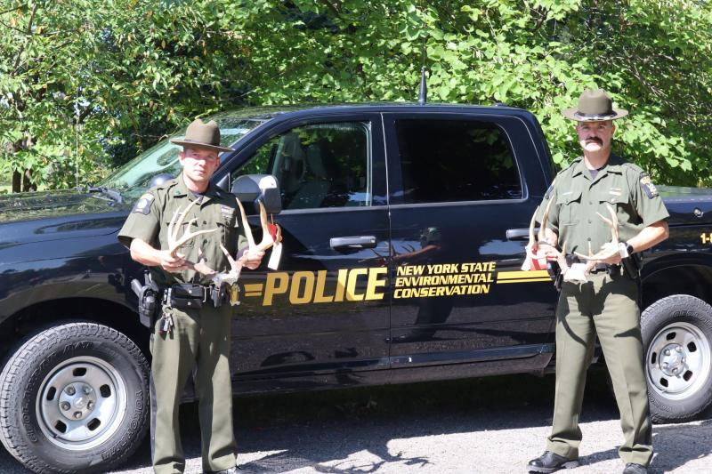 Two ECOs stand in front of patrol truck holding seized antler deer