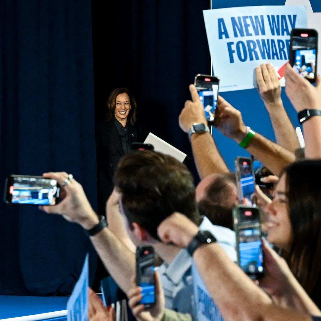 Kamala Harris at a campaign event in Pennsylvania, with roughly a dozen people in the foreground, most holding up cameras to record her.