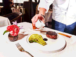A GIF of a person pouring sauce next to a plated steak.