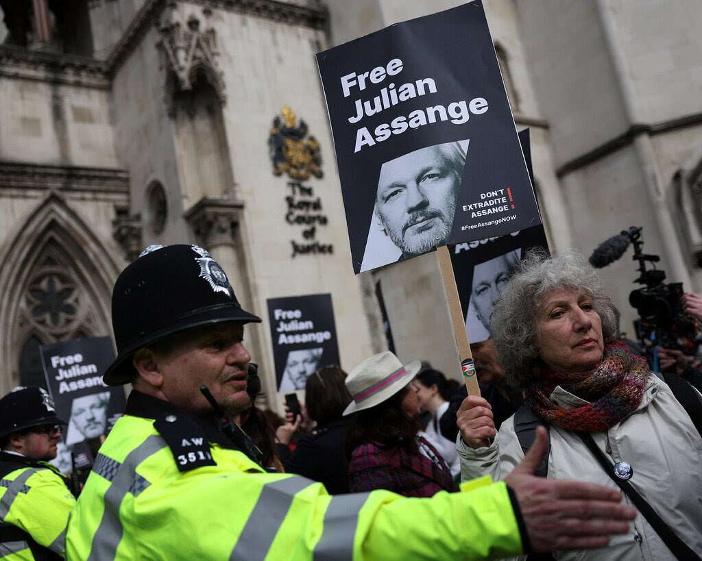 Police officers stand near people carrying signs supporting WikiLeaks founder Julian Assange.