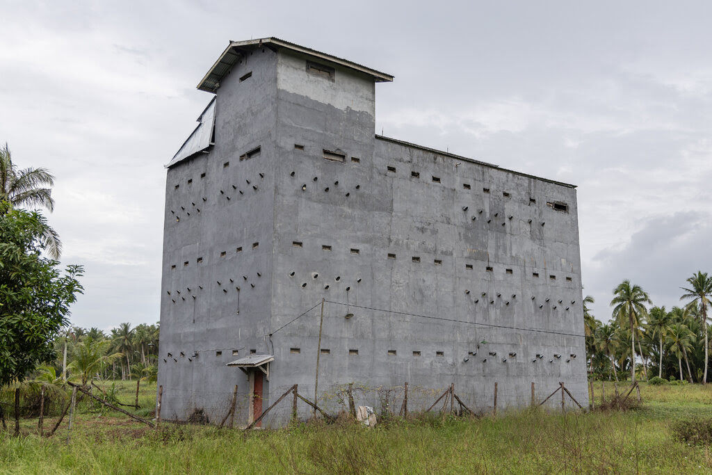 A multistory concrete structure with many small round and rectangular holes sits in a green field. 