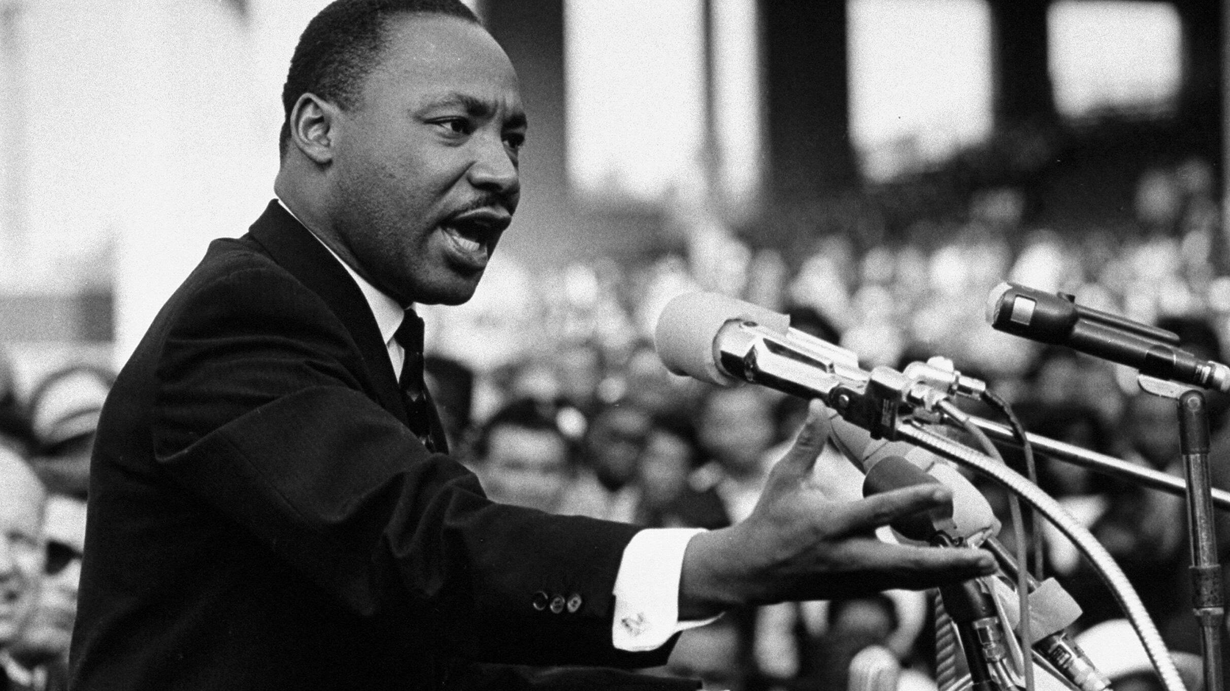 Black & white photo of Rev. Martin Luther King, Jr. speaking to a packed crowd.