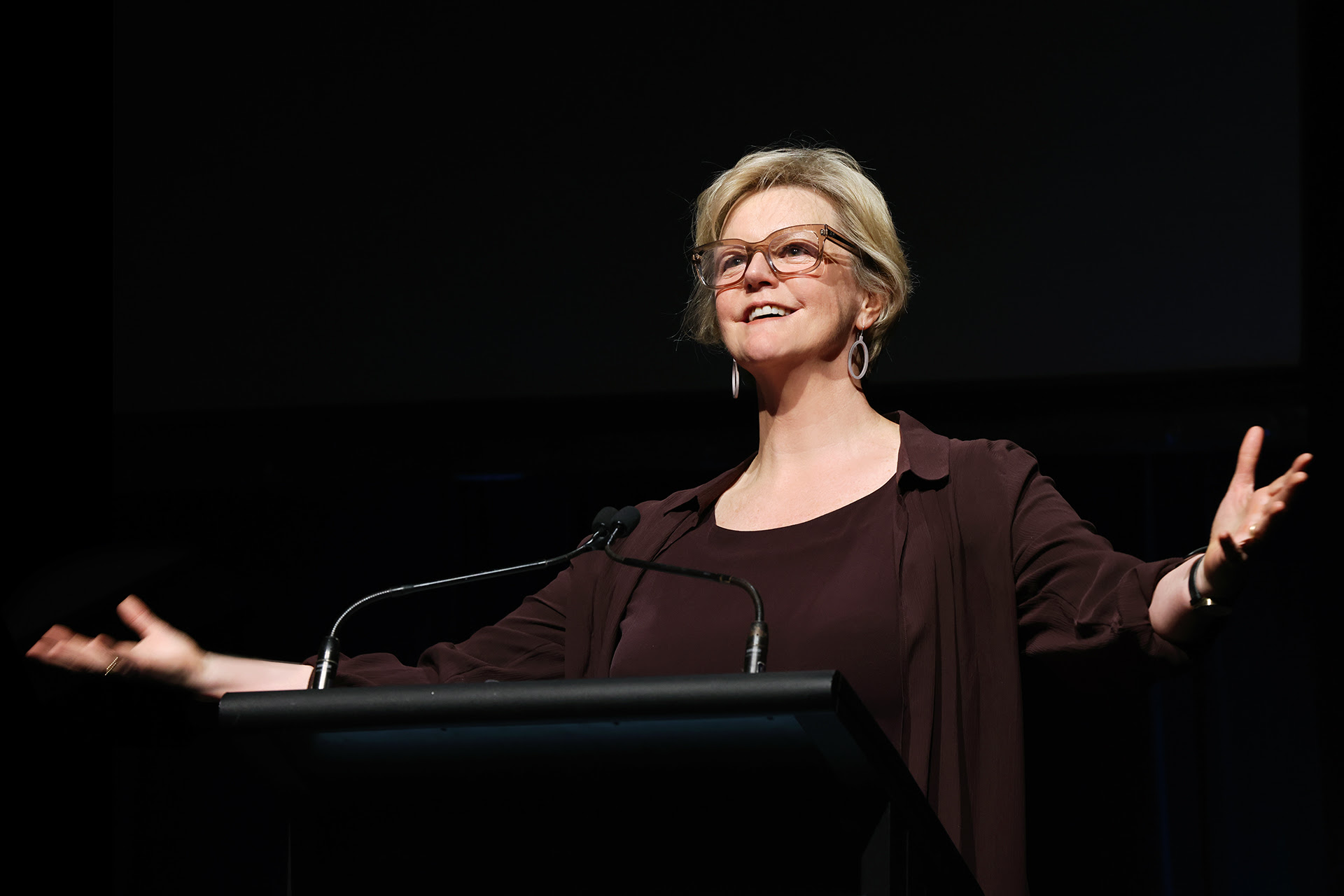 A woman at a lectern with her arms spread