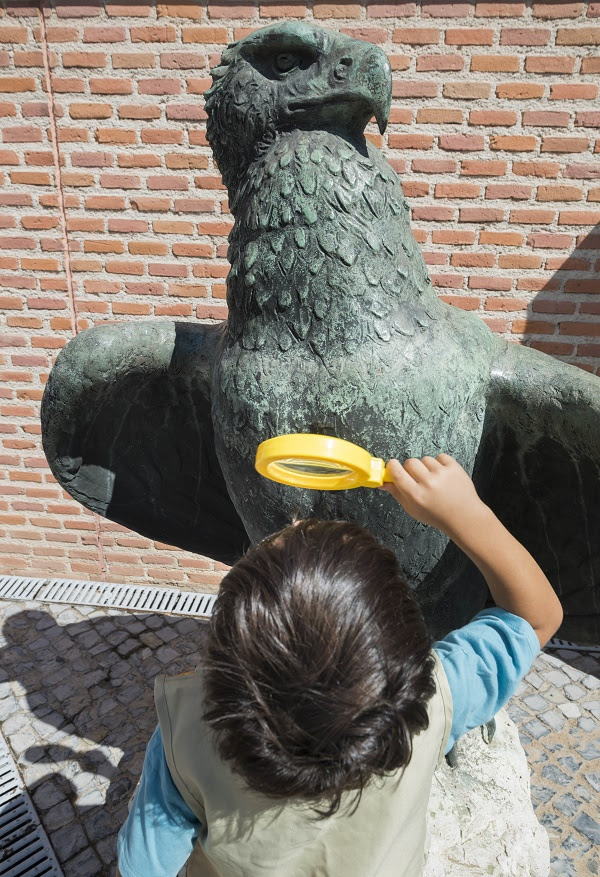 niño mirando con lupa una escultura de un águila