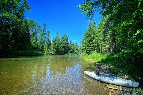 A kayak and paddle rest on a sandbar in the middle of the Rifle River.
