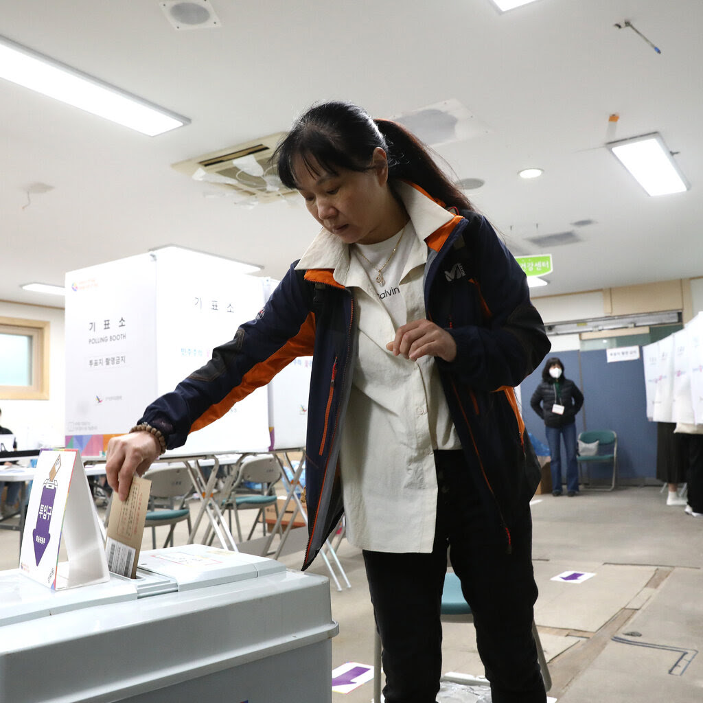A person in a blue and orange jacket casts an early vote at a polling station for the parliamentary election in South Korea.