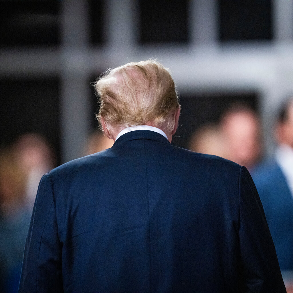 Donald Trump, wearing a navy suit, walks with his back to the viewer.